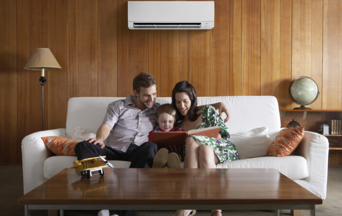 Parents sitting on a couch reading to their son in a living room.