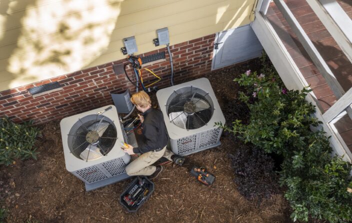 A service technician working on a HVAC unit outside of a residential home.